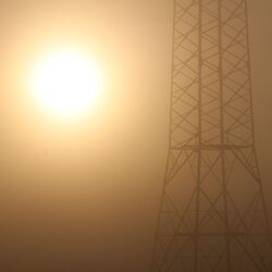 Surreale Szenerie mit bräunlich-orangefarbenem Himmel, links die grelle diffuse Sonne, rechts ein unscharfer Strommast im Nebel.